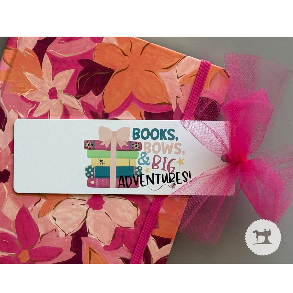 Floral-patterned product with a pink bow and a tag reading 'Books, Bows, & Big Adventures!'.