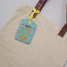Beige tote bag with a decorative tag on a light background