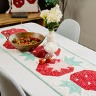 Table setting with a decorative table runner featuring red and white patterns, accompanied by a bowl of salad and a glass of dessert.