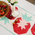 Table setting with strawberries, a bowl of strawberries, and a decorative tablecloth featuring star patterns.