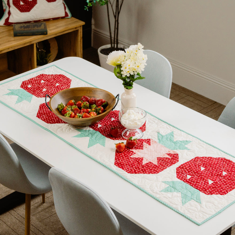 Dining table with a decorative table runner featuring red and green patterns, surrounded by chairs.