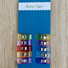 Pack of colorful clips on a blue card with 'my girlfriend's quilt shoppe' branding on a wooden surface.