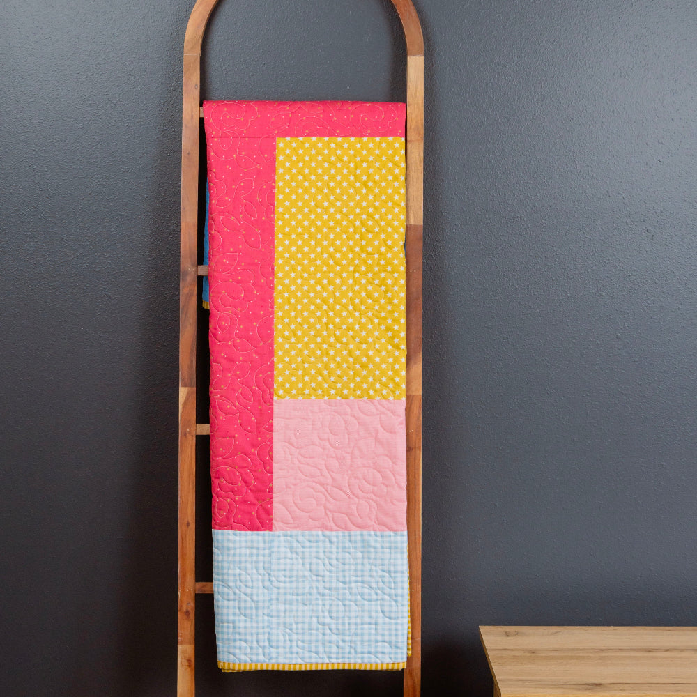 Colorful quilt on a wooden ladder against a dark wall