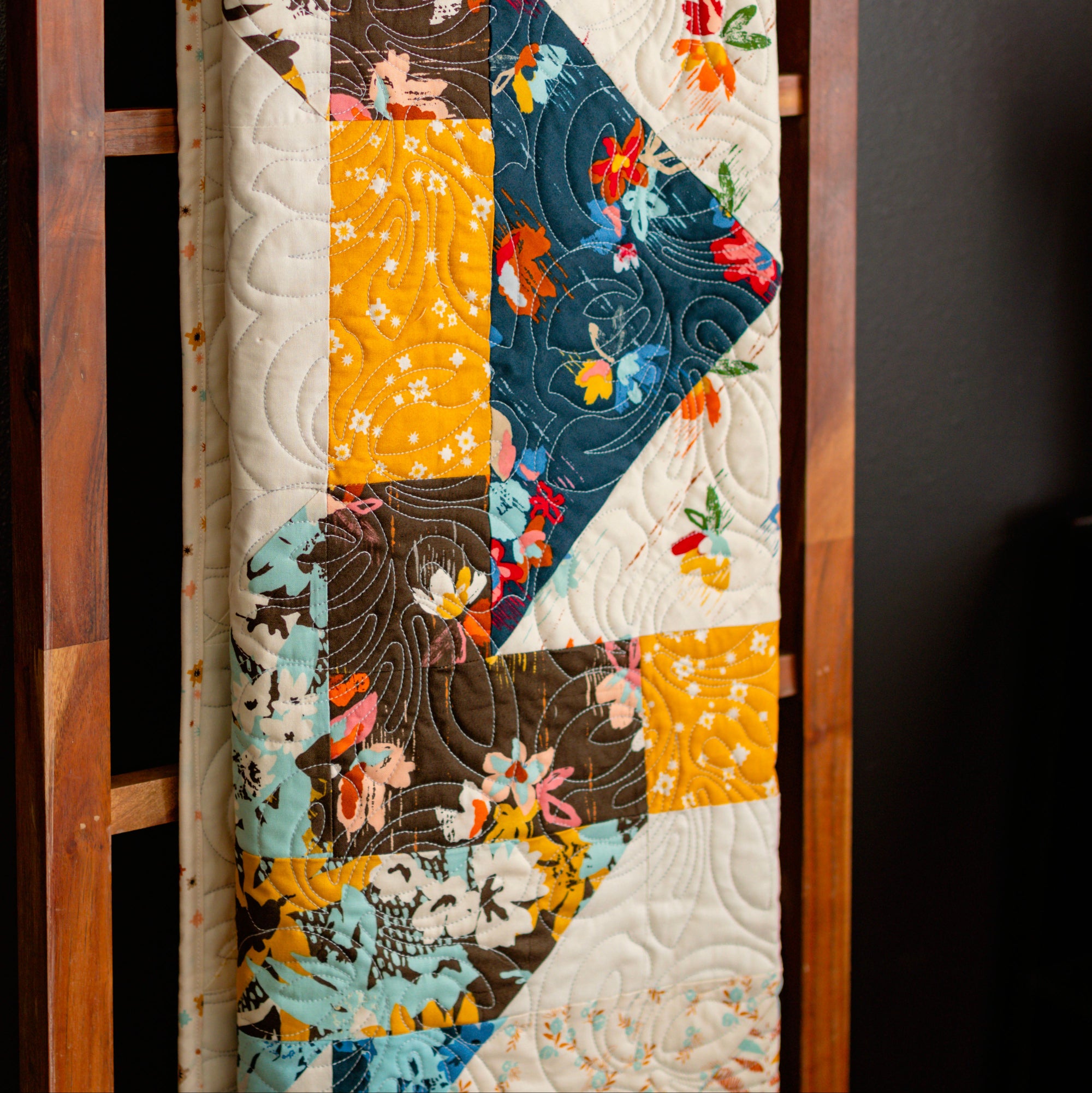 Colorful quilt with floral patterns displayed on a wooden frame against a dark background