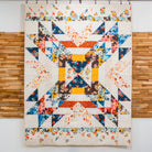 Colorful quilt with geometric pattern hanging on a wooden wall.