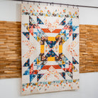 Colorful quilt with geometric patterns hanging on a wall.