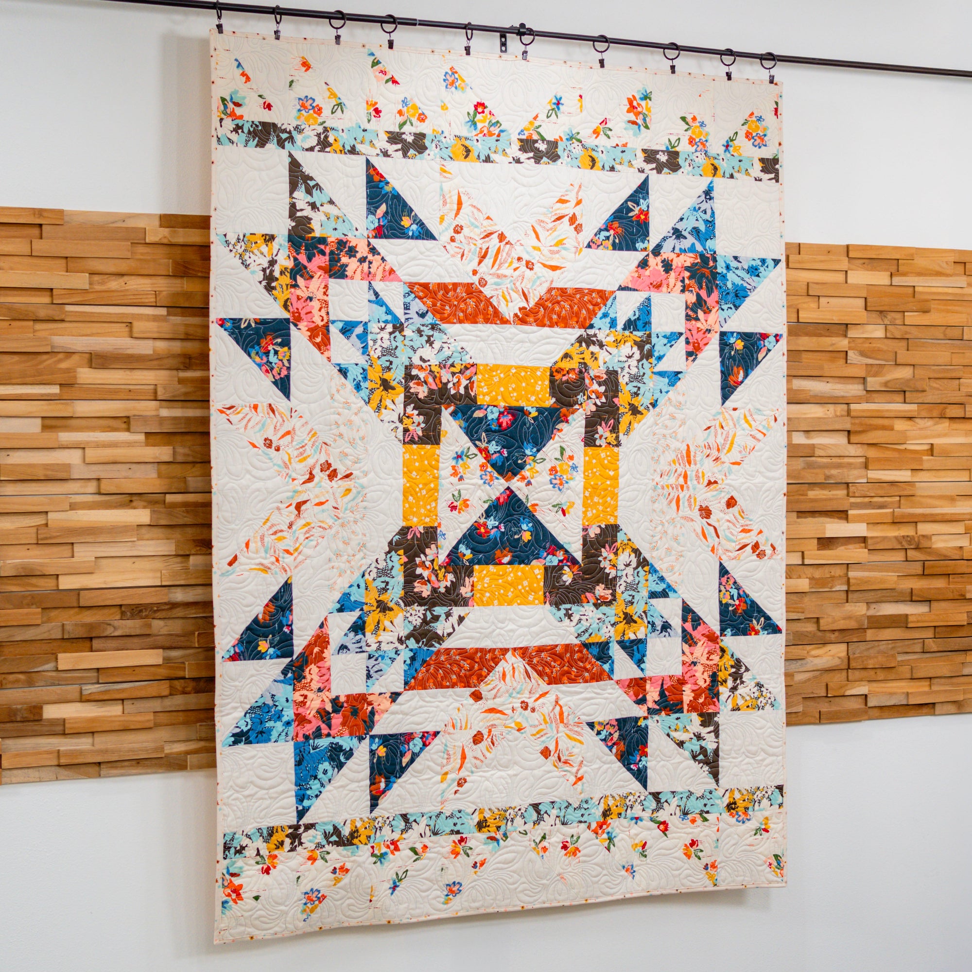 Colorful quilt with geometric patterns hanging on a wall.