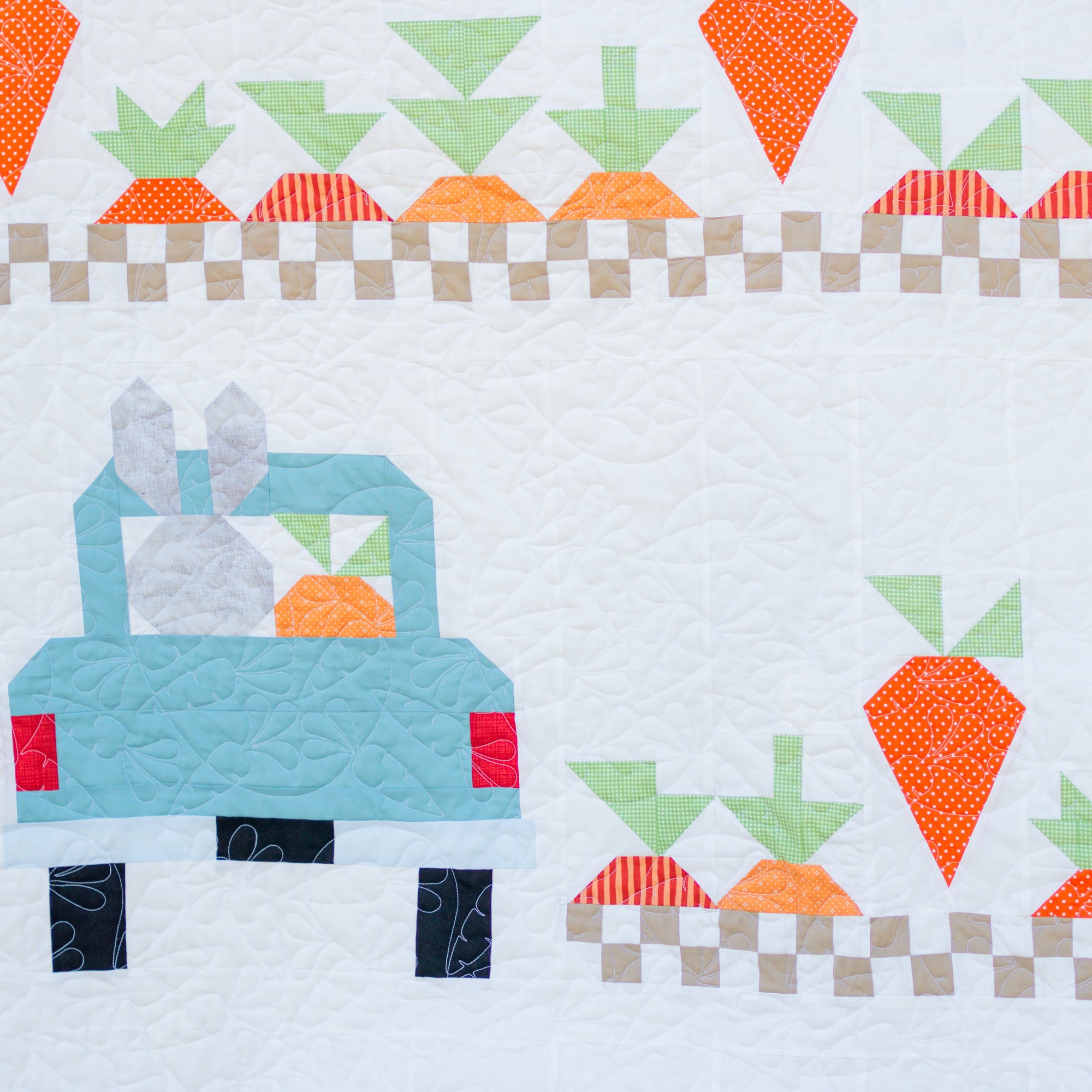 Quilt block with a blue truck and orange carrots on a white background