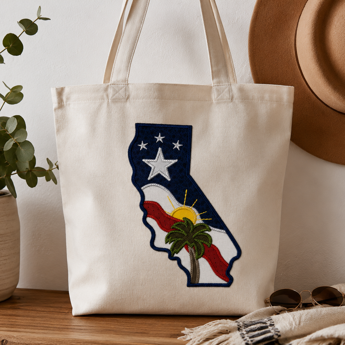 Tote bag with California design on a wooden surface with a plant and hat in the background
