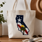 Tote bag with California design on a wooden surface with a plant and hat in the background