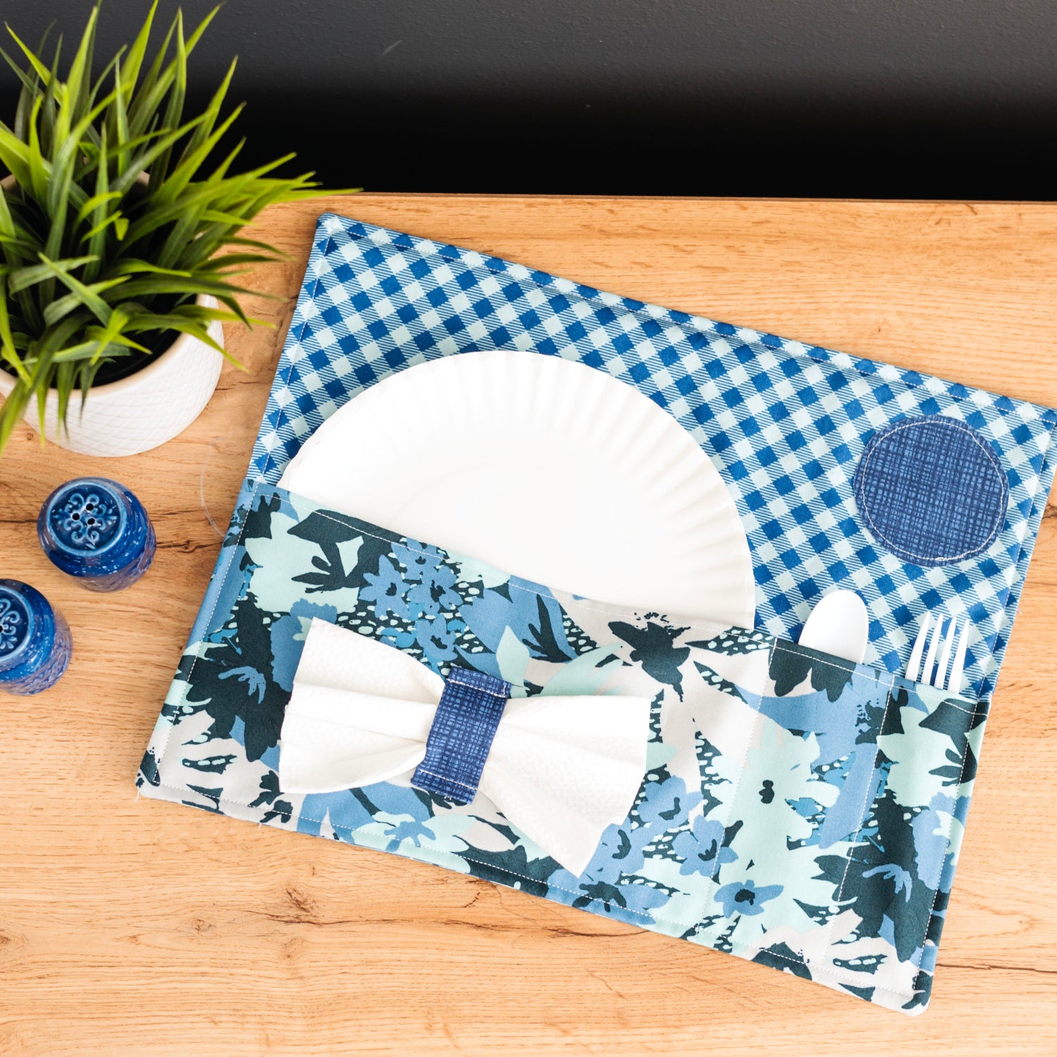 Placemat with blue and white design on a wooden table with a plant and small containers.