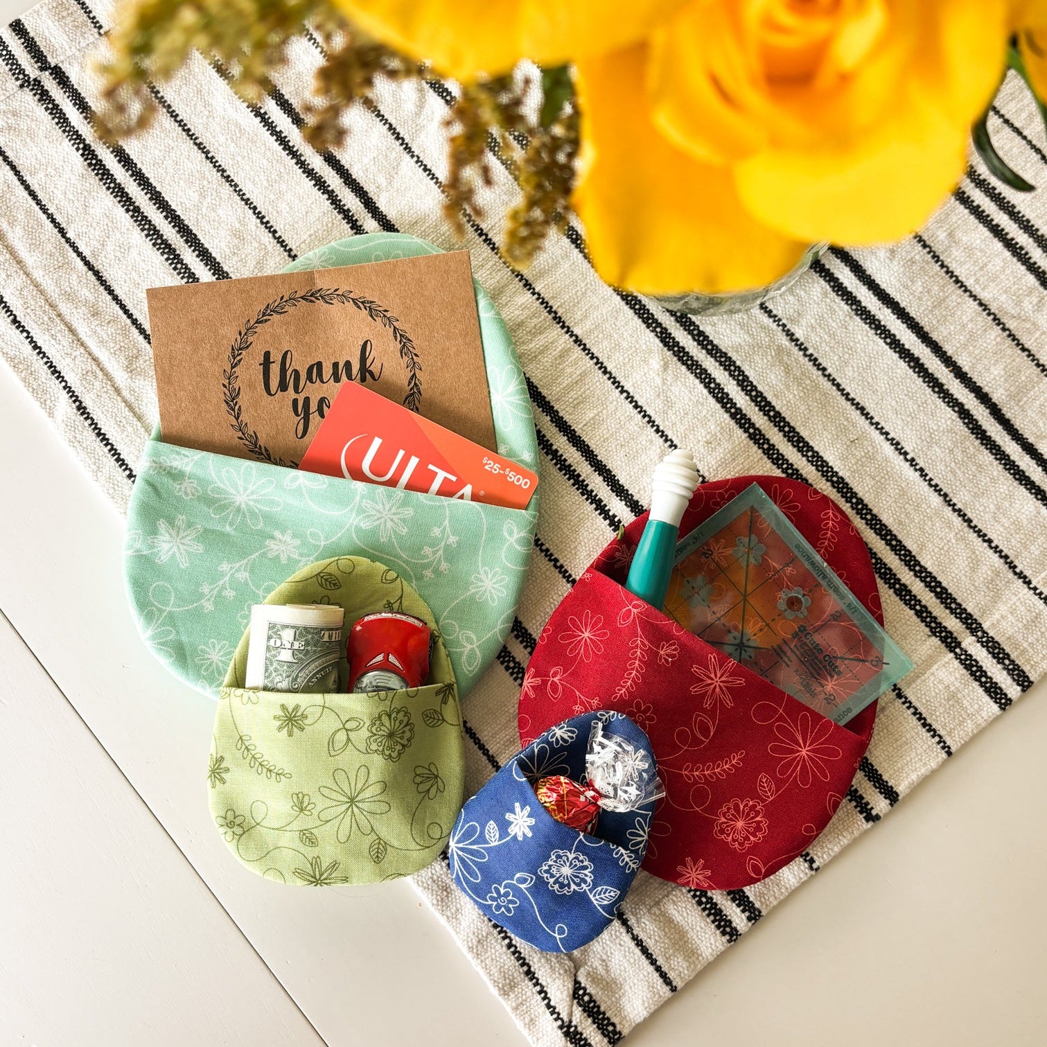 Small green fabric pouch with items on a striped surface with yellow flowers in the background