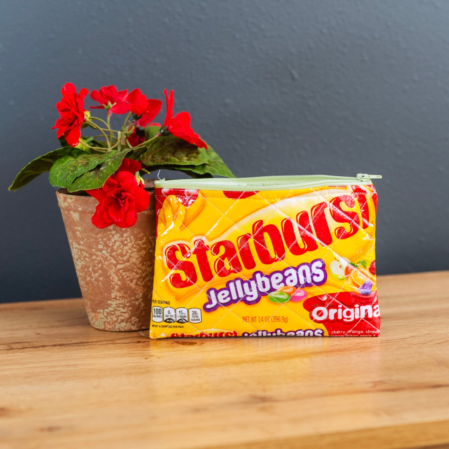 Starburst Jellybeans pouch on a wooden surface with a potted plant in the background