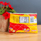 Packaged product with a yellow label on a wooden surface next to a potted plant.