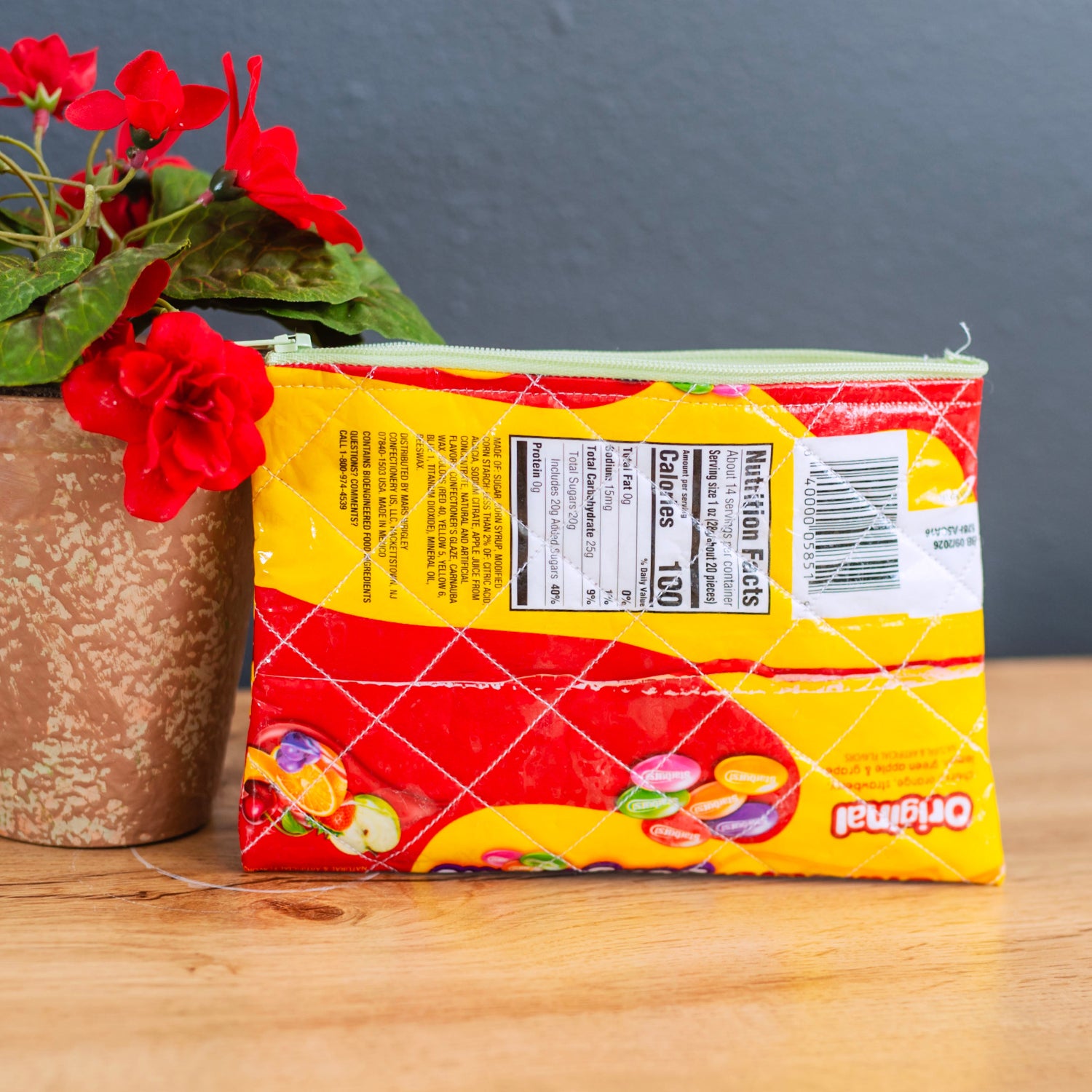 Packaged product with a yellow label on a wooden surface next to a potted plant.