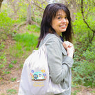Woman holding a drawstring bag with colorful designs in a forest setting
