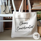 Beige tote bag with 'Chaos Coordinator' text on a blurred indoor background