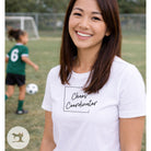 Woman wearing a white t-shirt with 'Chaos Coordinator' text on a soccer field.