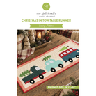 Sewing pattern cover for 'Christmas in Tow Table Runner' by my girlfriend's [quilt shoppe]. The cover features a photo of a finished quilted runner with three colorful train cars (green, light blue, red) on a white background with a red border, styled on a wooden table with holiday decorations.