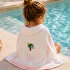 Child sitting by a pool with a towel draped over them, featuring a palm tree design.