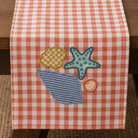 Red and white checkered table runner with embroidered beach-themed designs on a wooden table.