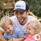 Man wearing a 'COOL DAD' cap with two children outdoors
