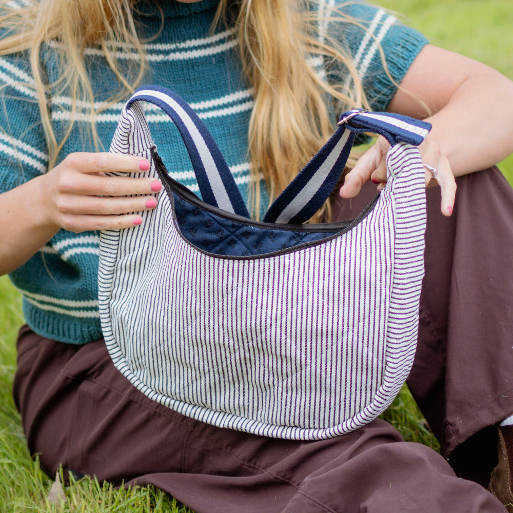 Person sitting on grass holding a striped bag