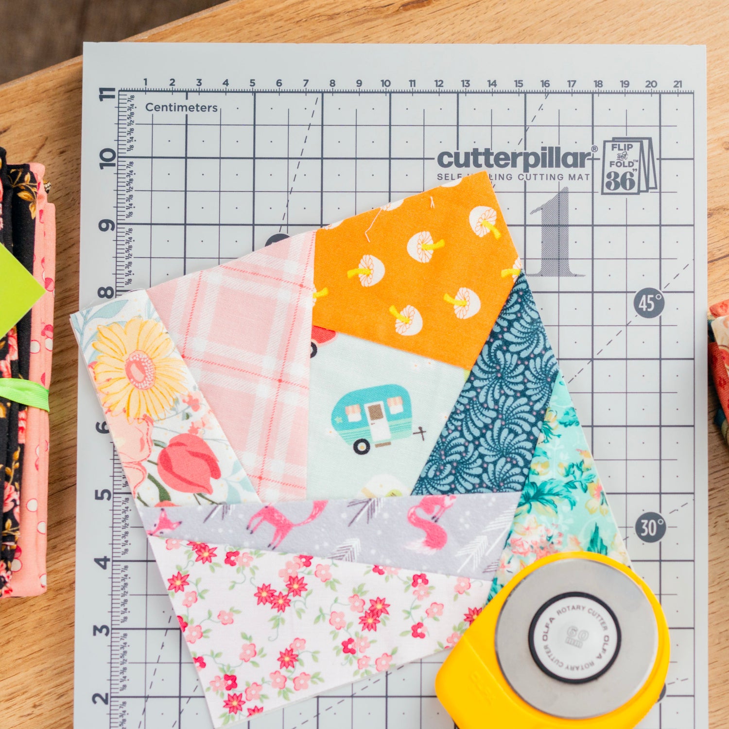 Fabric squares on a cutting mat with a rotary cutter, on a wooden surface.