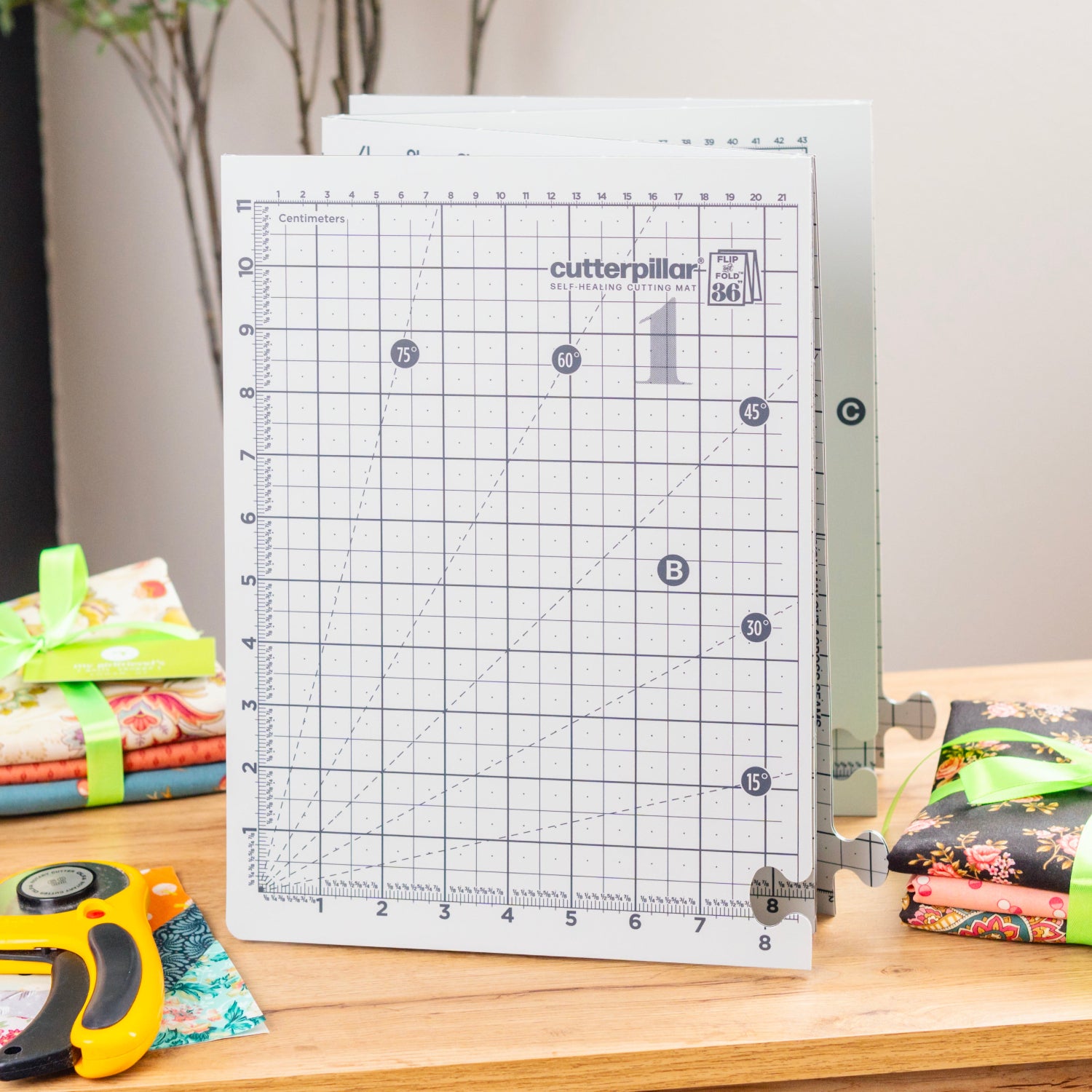 Grid cutting mat on a table with fabric stacks and a rotary cutter in the background