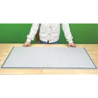 Person standing behind a large grid mat on a wooden surface with a green background
