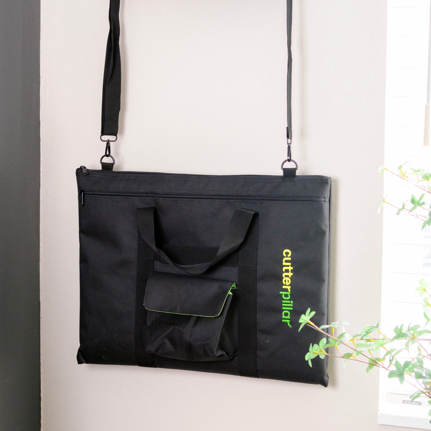 Black bag with a handle hanging on a wall-mounted hook against a white wall.