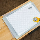 Glow in the Dark cutting mat with grid lines on a wooden surface, accompanied by a rotary cutter.