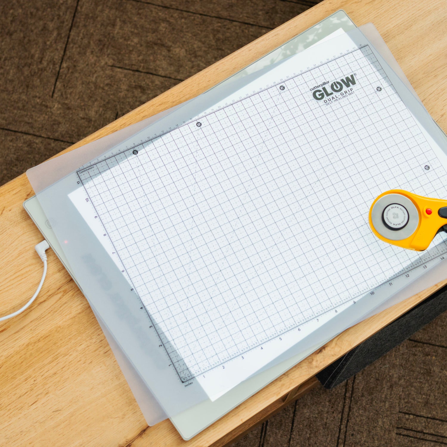 Glow in the Dark cutting mat with grid lines on a wooden surface, accompanied by a rotary cutter.