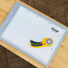Grid cutting mat with a rotary cutter on a wooden surface, featuring the brand 'Glow'.