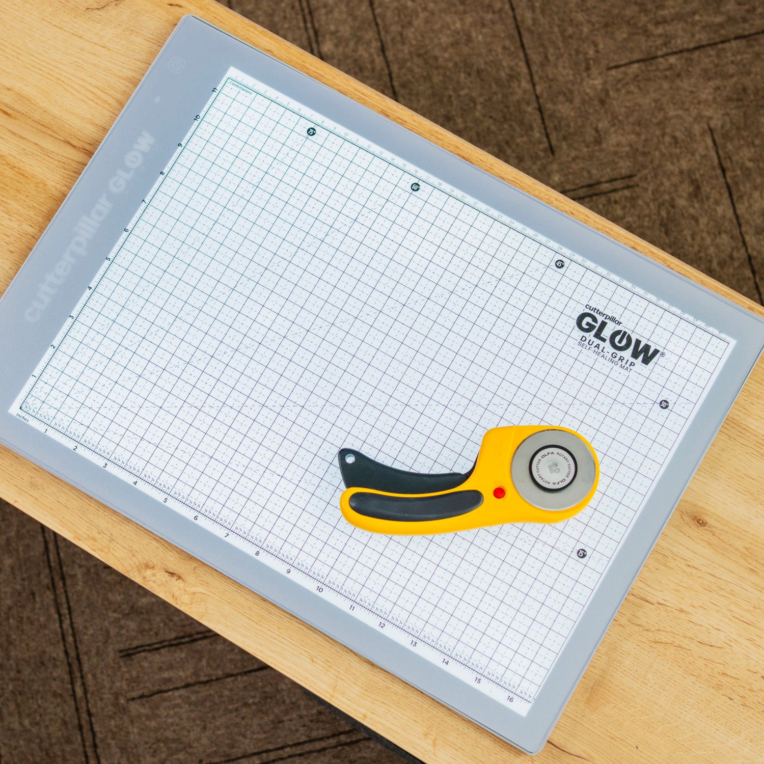 Grid cutting mat with a rotary cutter on a wooden surface, featuring the brand 'Glow'.