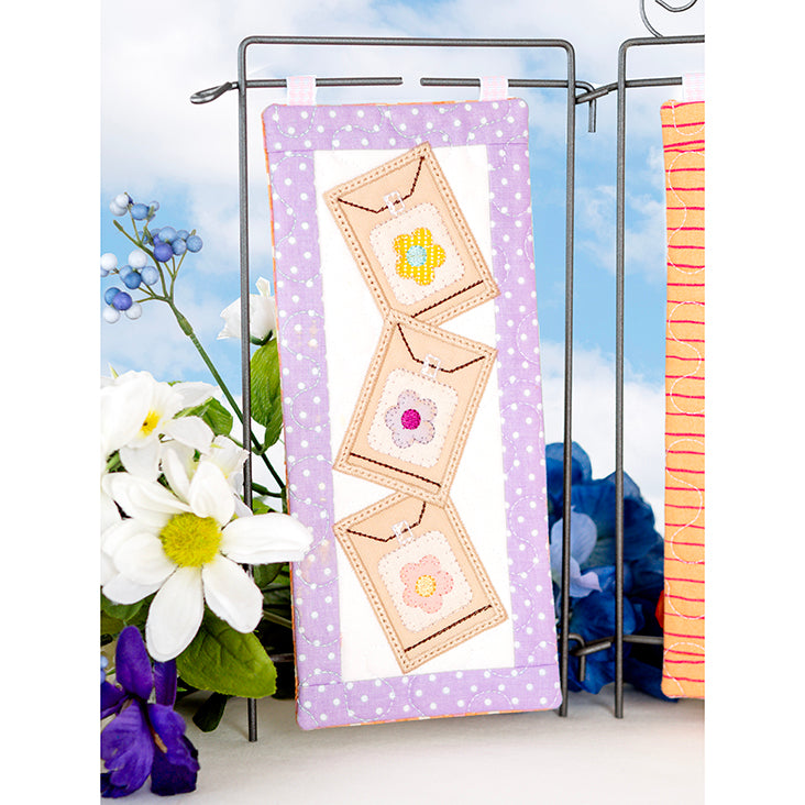 Decorative wall hanging with floral designs on a stand, surrounded by flowers.