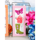 Decorative towel with gardening-themed design featuring a butterfly, watering can, and boots on a checkered background.
