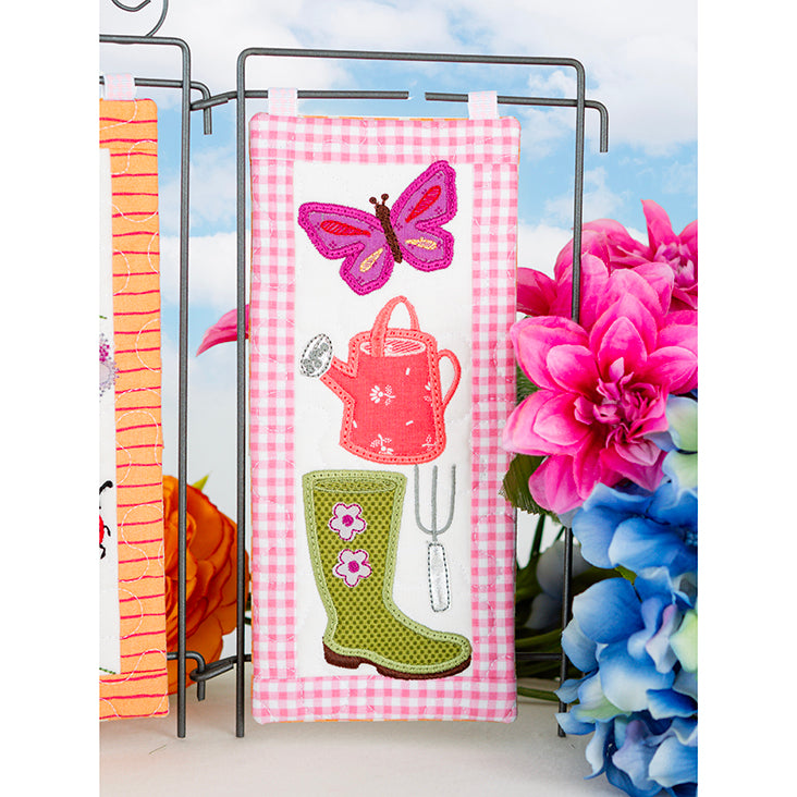 Decorative towel with gardening-themed design featuring a butterfly, watering can, and boots on a checkered background.