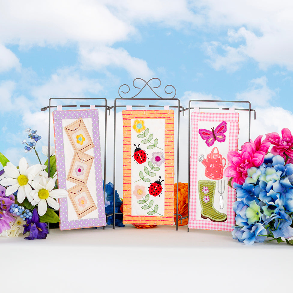 Three decorative cards with floral and nature-themed designs on a stand against a blue sky background.