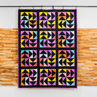 Colorful geometric quilt hanging on a rack against a wooden wall.