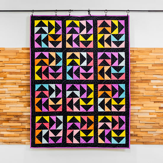 Colorful geometric quilt hanging on a rack against a wooden wall.