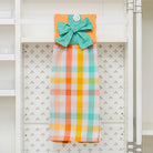 Colorful plaid towel with a green bow hanging on a rack against a white wall.