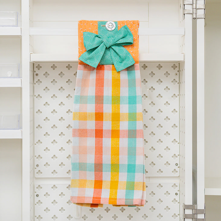 Colorful plaid towel with a green bow hanging on a rack against a white wall.