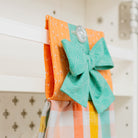 Colorful fabric bow hanging on a pegboard with an orange towel.