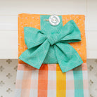 Fabric square with a green bow and button on an orange background