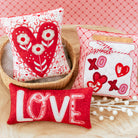 Three decorative pillows with heart and 'LOVE' designs on a red checkered background.