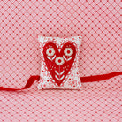 Decorative pillow with heart design and red ribbon on a pink grid background