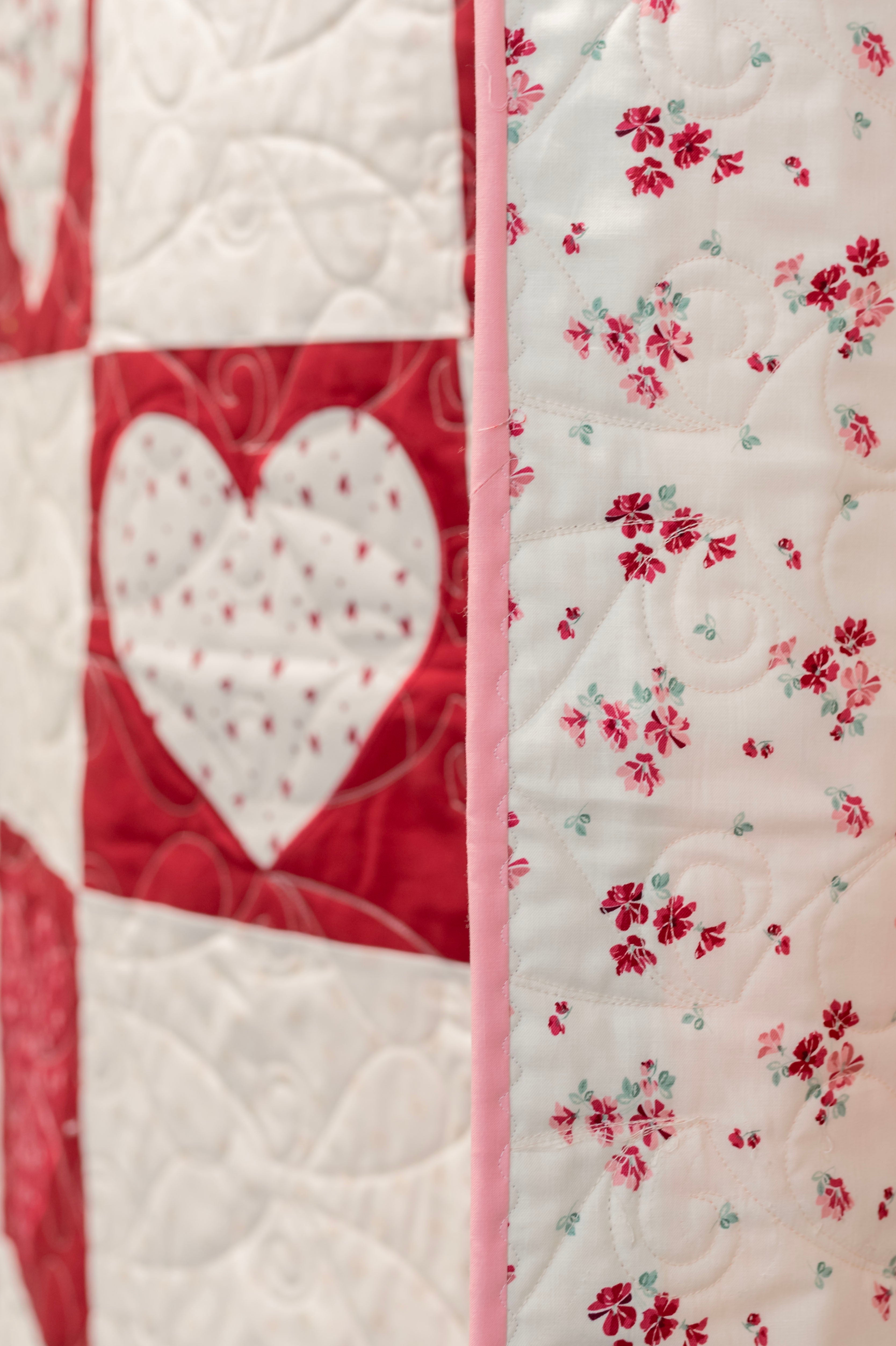 Quilt with heart and floral patterns in red, white, and pink.