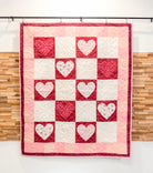 Quilt with heart pattern hanging against a wooden panel background