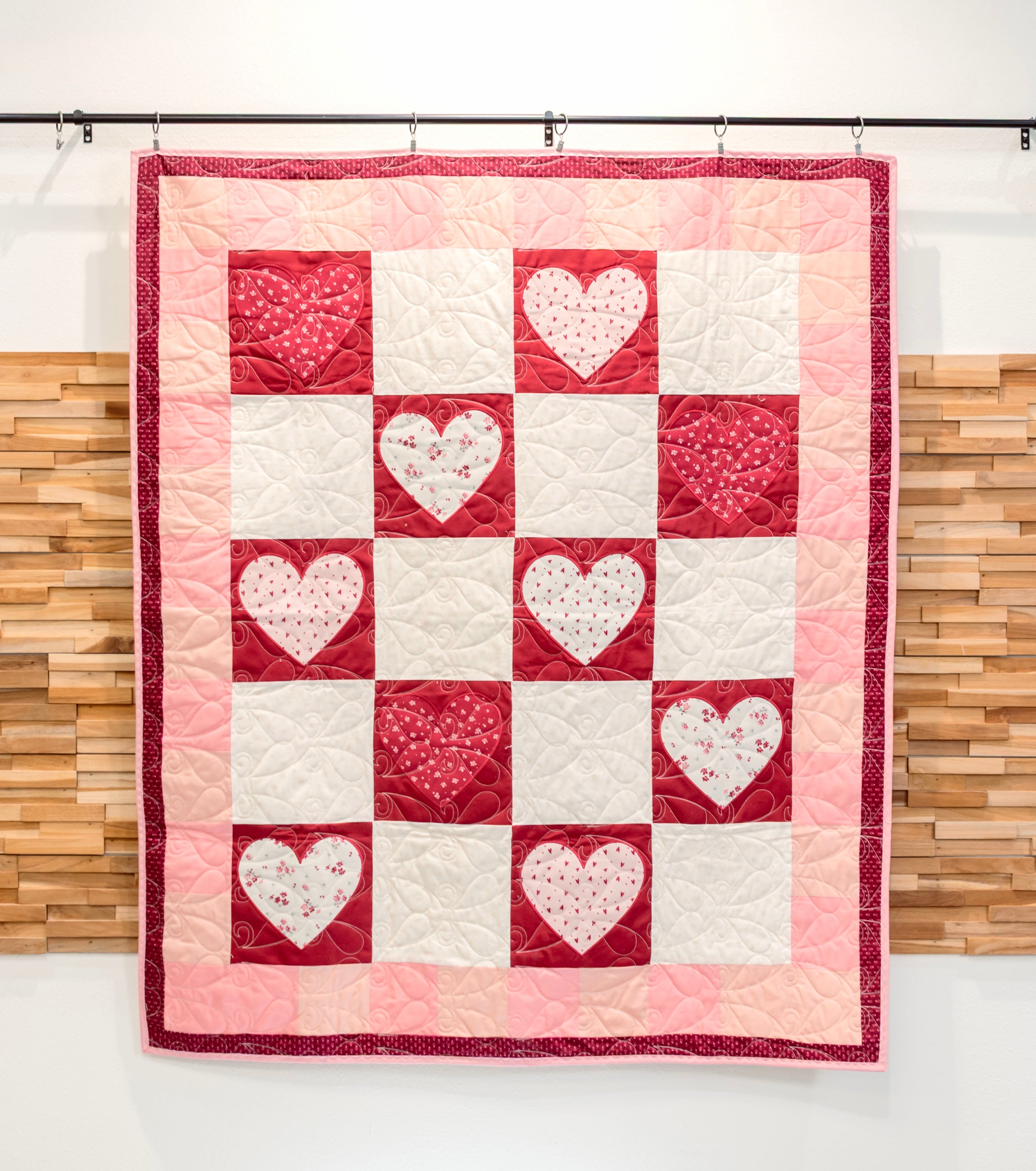Quilt with heart pattern hanging against a wooden panel background